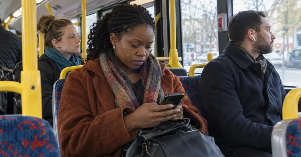 A bus passenger looks at a phone while other commuters and the street outside remain in view